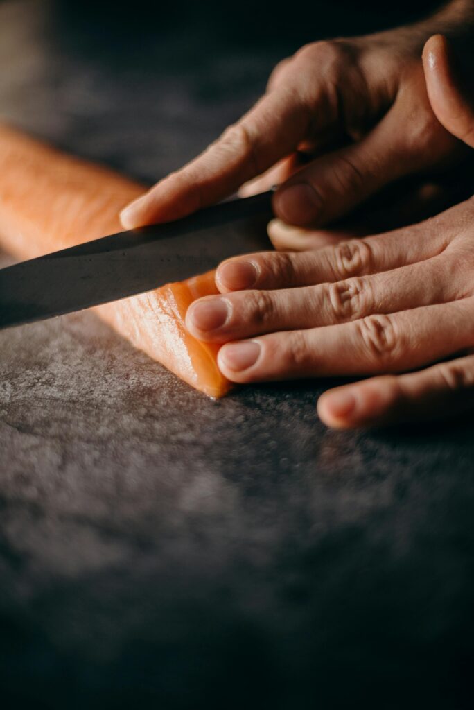 Close-up of hands skillfully slicing fresh salmon fillet for delicious Japanese cuisine.